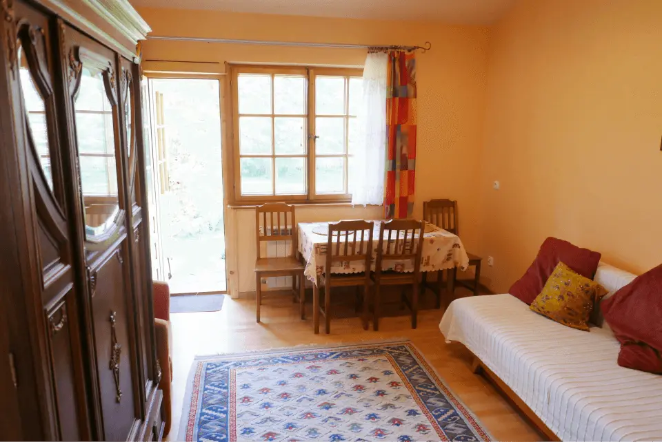 Pokój ze stolikiem, dywanem oraz wyjściem na zewnątrz w kierunku ogrodu, w pokoju znajduje się również szafa i łóżko