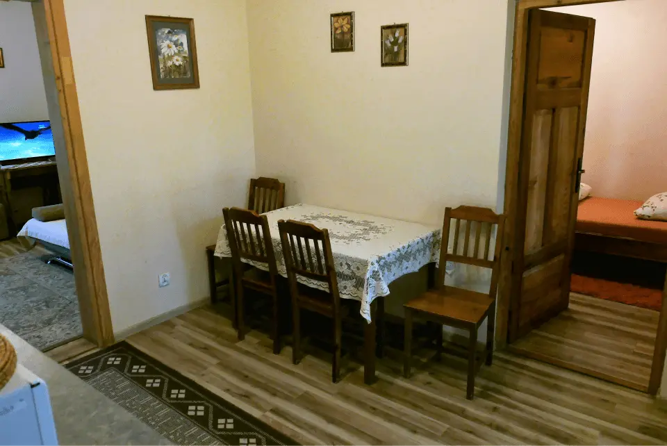 Apartament pod modrzewiem, na zdjęciu widzimy stół z 4 krzesłami oraz wejścia do poszczególnych pokoi tego apartamentu